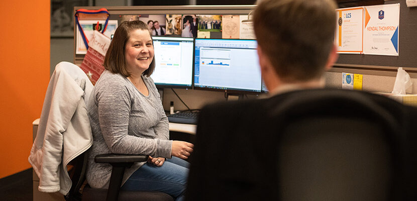 Woman sitting at office desk talking to coworker