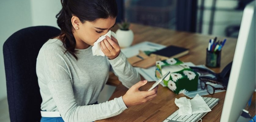 Woman staying healthy at work blowing her nose at her desk