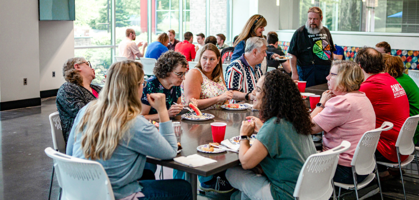 A group of people sitting down at a lunch table on their lunch break eating and talking.